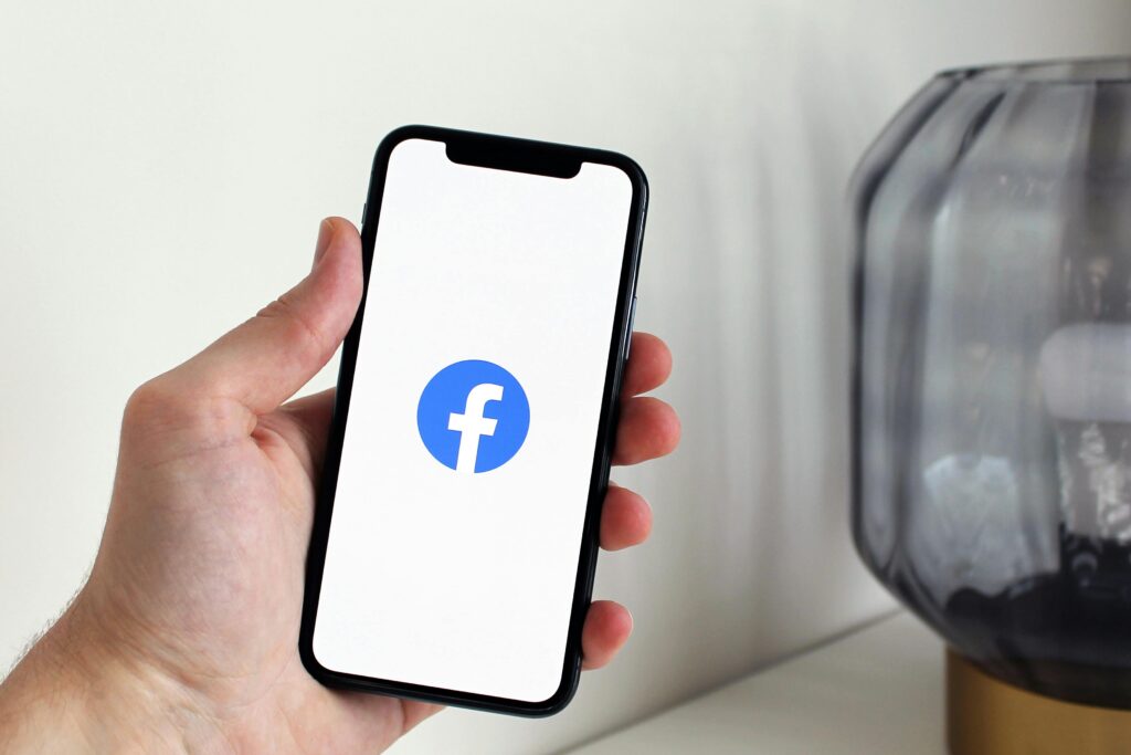Close-up of a hand holding a smartphone displaying the Facebook logo indoors.